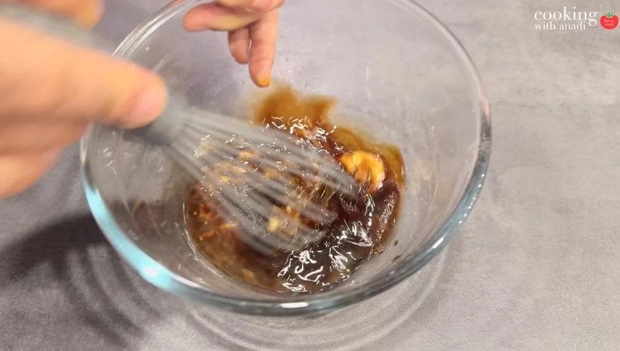 Whisking a dark marinade with lemongrass, soy sauce, and oyster sauce in a glass bowl.