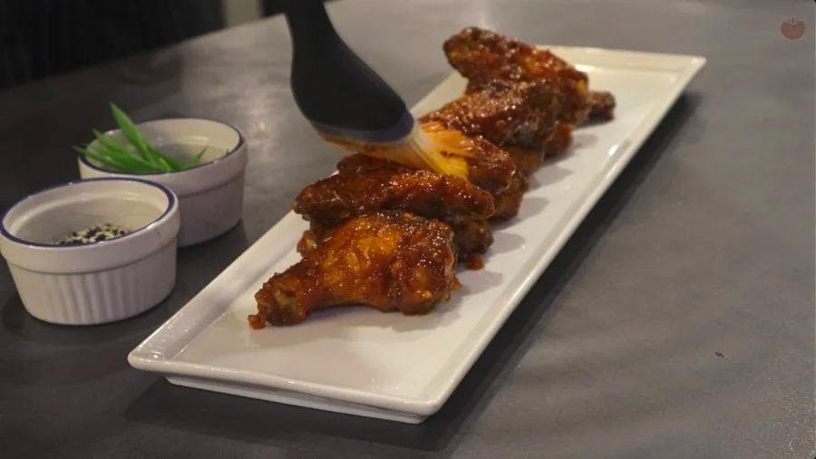 Glazed Korean fried chicken wings arranged on a white rectangular plate with sesame seeds and dipping sauces.