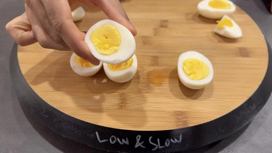 Hard boiled eggs halved on a bamboo cutting board labeled "Low & Slow"