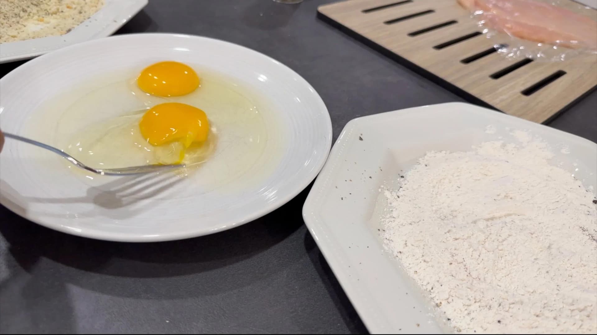 Three breading station bowls: whisked eggs in white bowl with fork, flour, and panko breadcrumbs for schnitzel preparation.