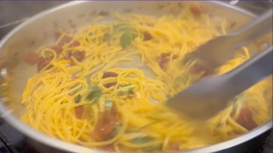 Spaghetti being tossed with lemon sauce, salmon, and fresh parsley in a pan with wooden utensils.
