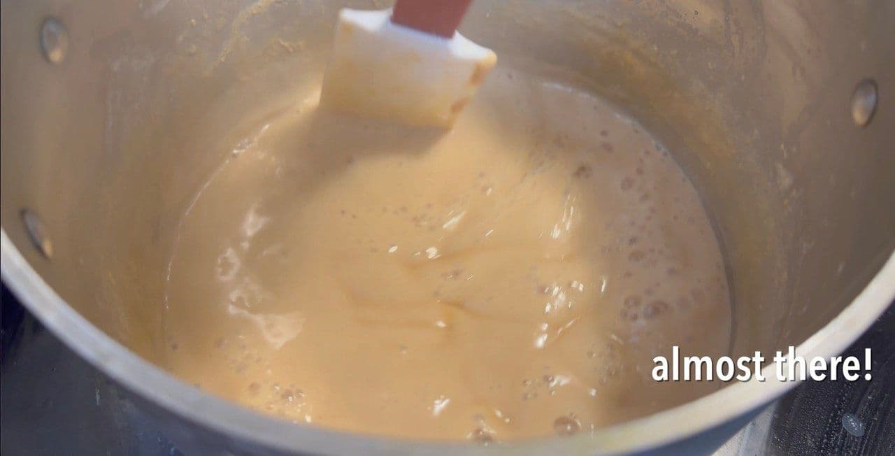 Thickened lactose-free condensed milk in a pot with a spatula, nearly ready to transfer to a jar.