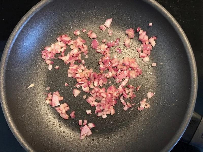 Diced ham or bacon cooking in a dark non-stick pan with oil.