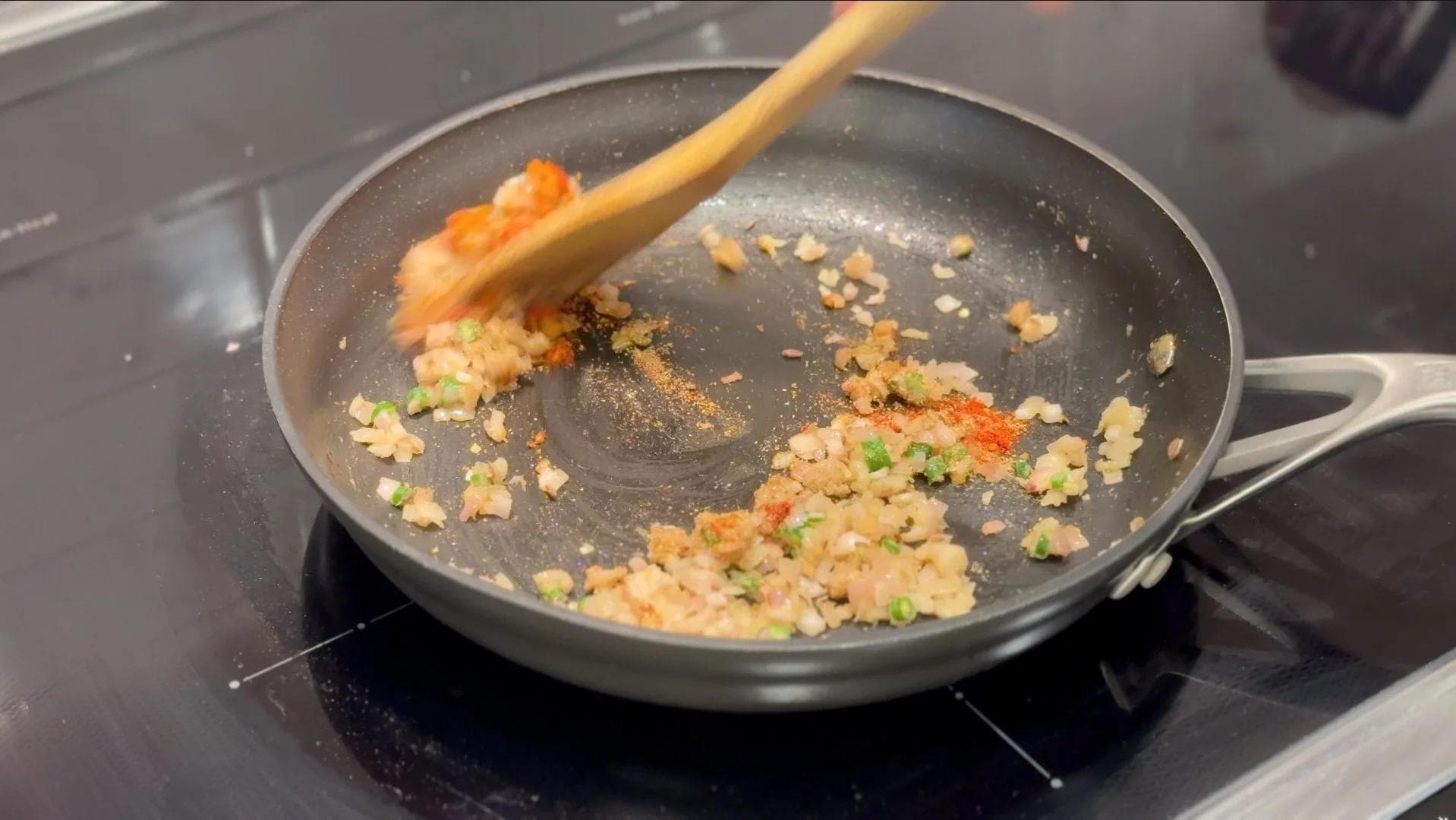 Sautéing diced vegetables and spices in a wok with a wooden spoon on a stovetop.
