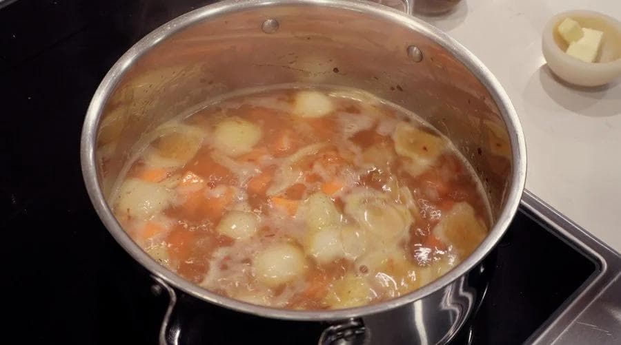 Pot of simmering carrot and ginger soup with tender carrots and potatoes in broth on stovetop.