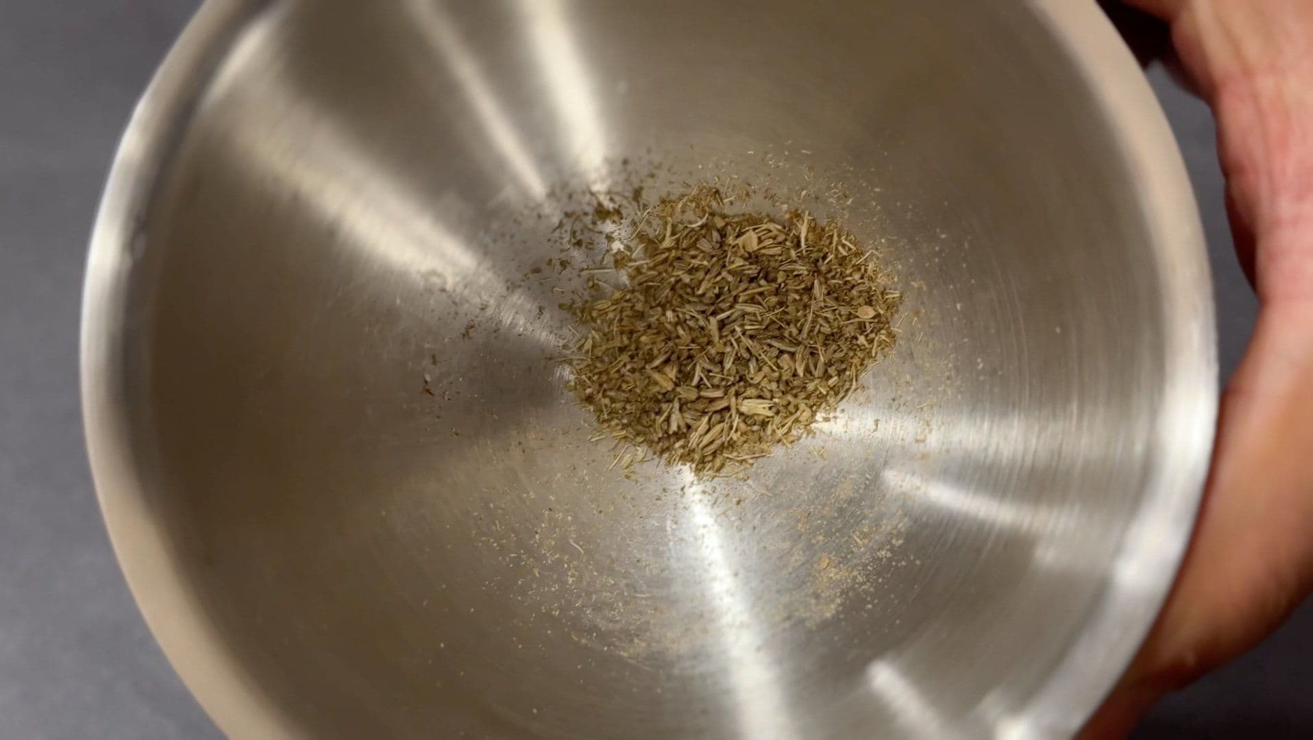 Crushed fennel and anise seeds in a stainless steel bowl during sausage preparation.
