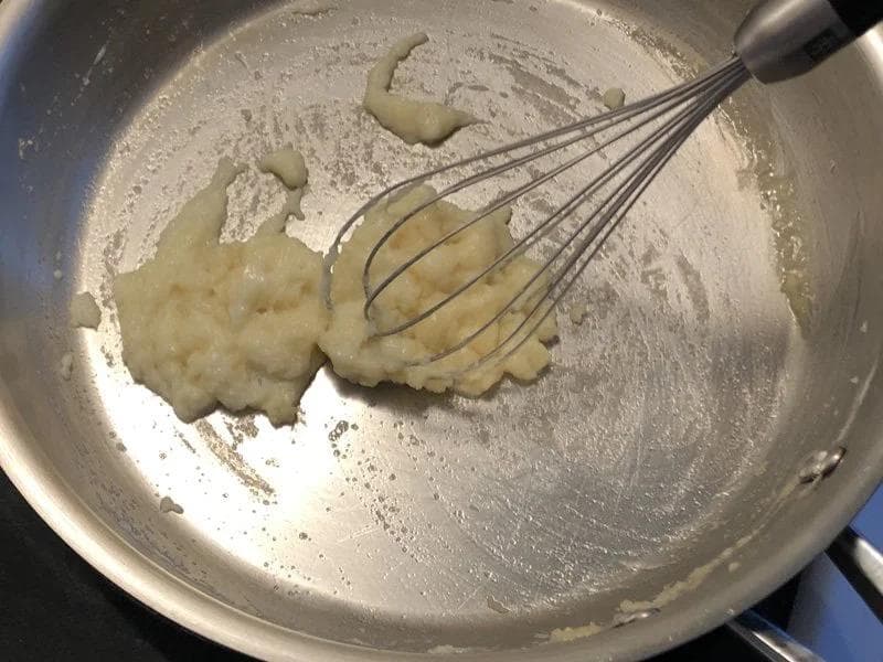 Whisking flour and butter roux in a metal pot while gradually adding milk to make béchamel sauce.