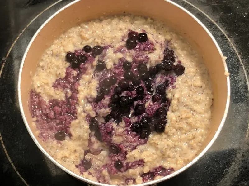 Oatmeal mixture with blueberries and chia seeds stirred in, showing purple-tinted oats in a white bowl.