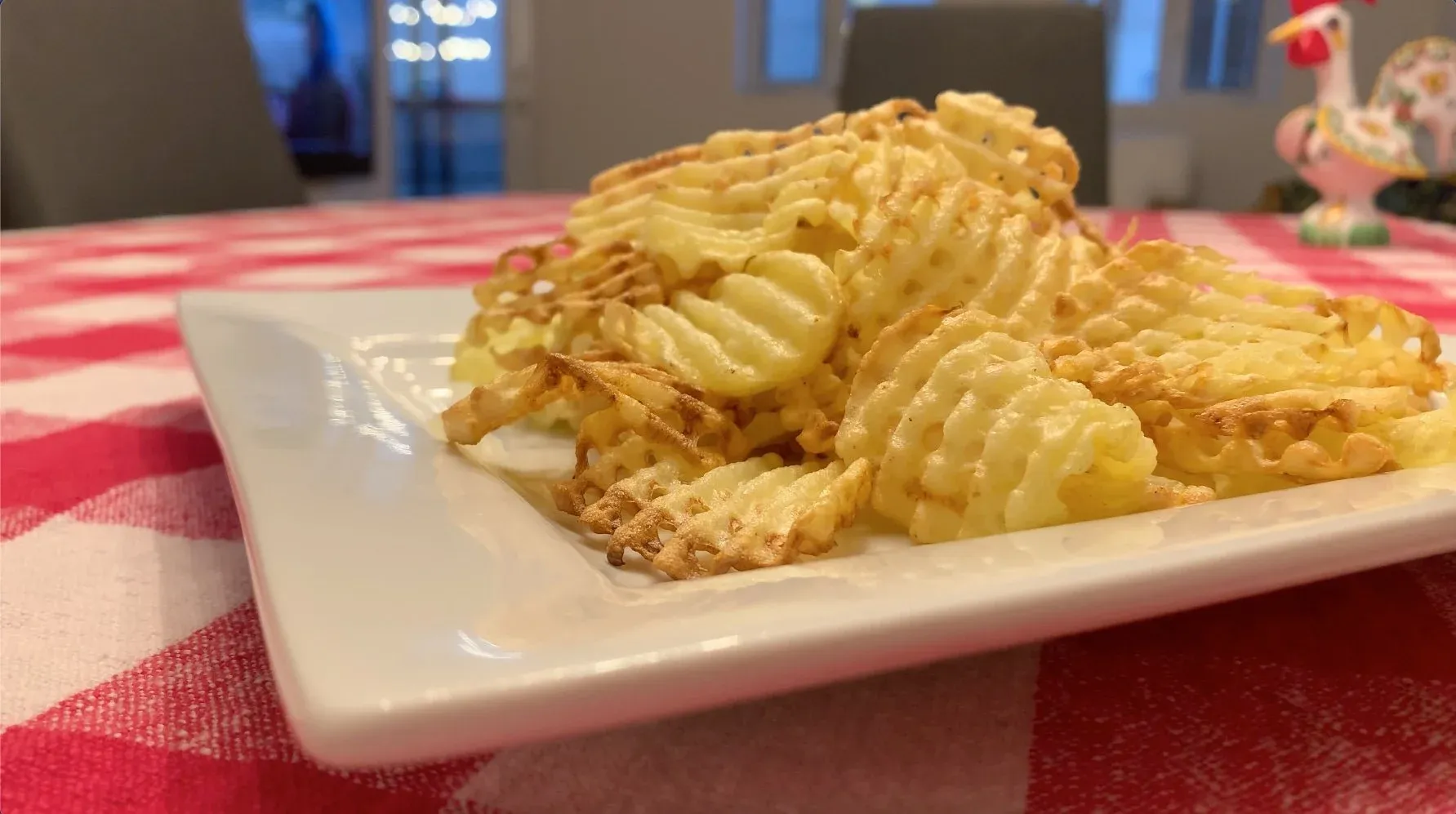 Golden waffle fries piled on a white rectangular plate atop a red and white checkered tablecloth.