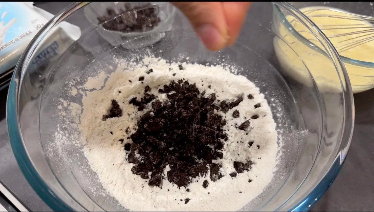 Crushed Oreo cookie pieces mixed into white dry pancake batter in a glass bowl