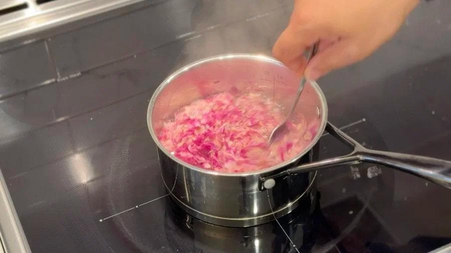 Rose petals simmering in water in a saucepan, turning the liquid pink for rose syrup.
