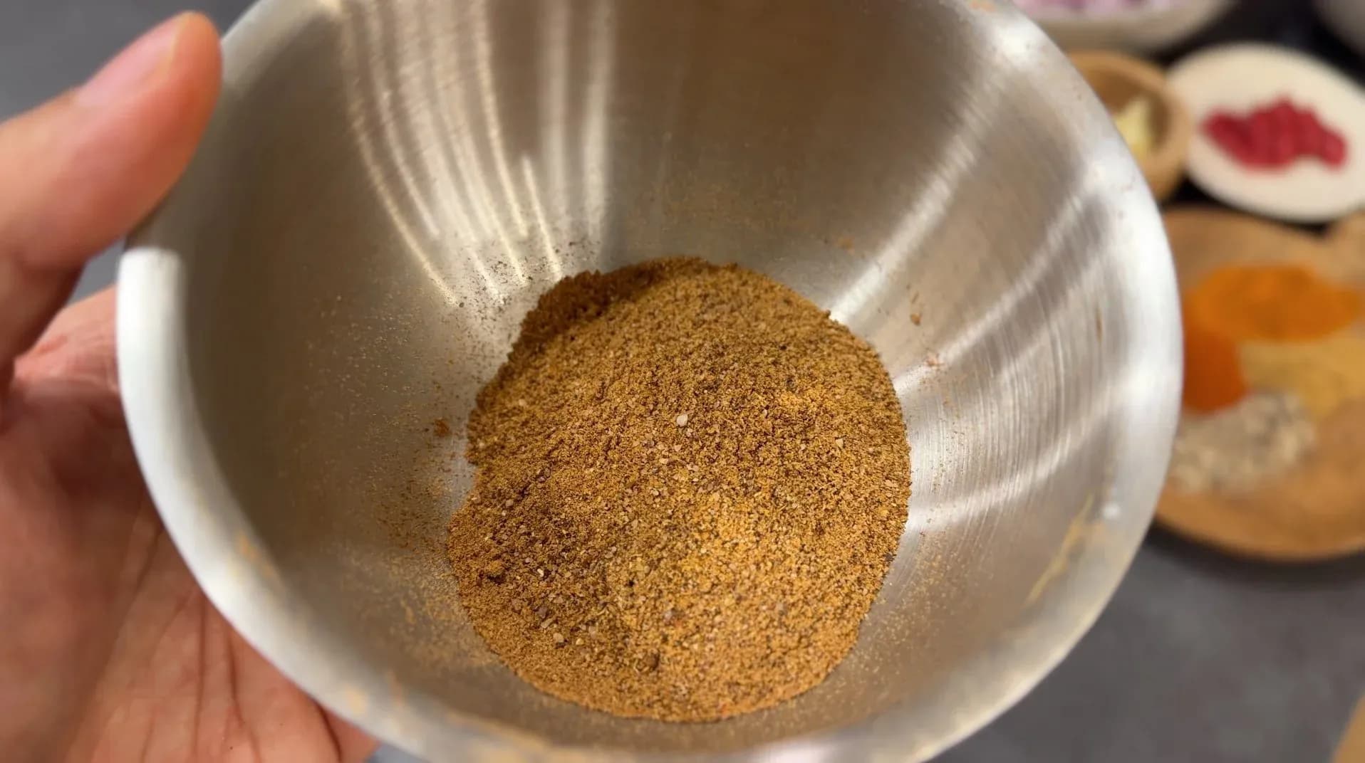 Ground spice mixture for recado paste in a white bowl held in hand