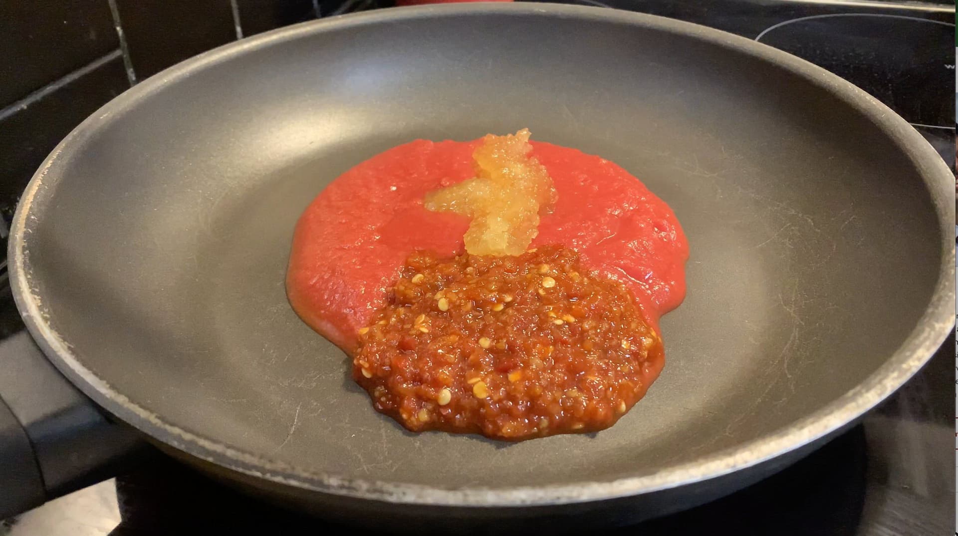 Red sauce and minced garlic mixture simmering in a gray pan on stovetop.