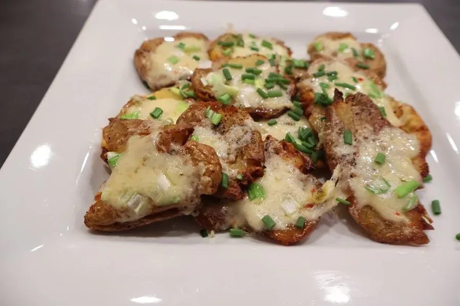 Crispy air fryer smashed potatoes topped with melted cheese and fresh green onions on a white plate.