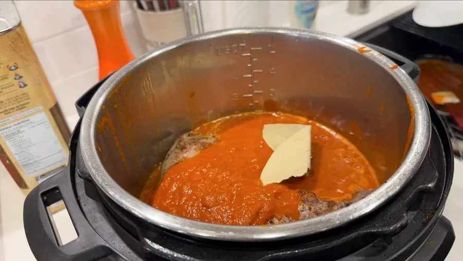 Instant Pot filled with red birria consommé and meat slow cooking on low heat with butter on top.