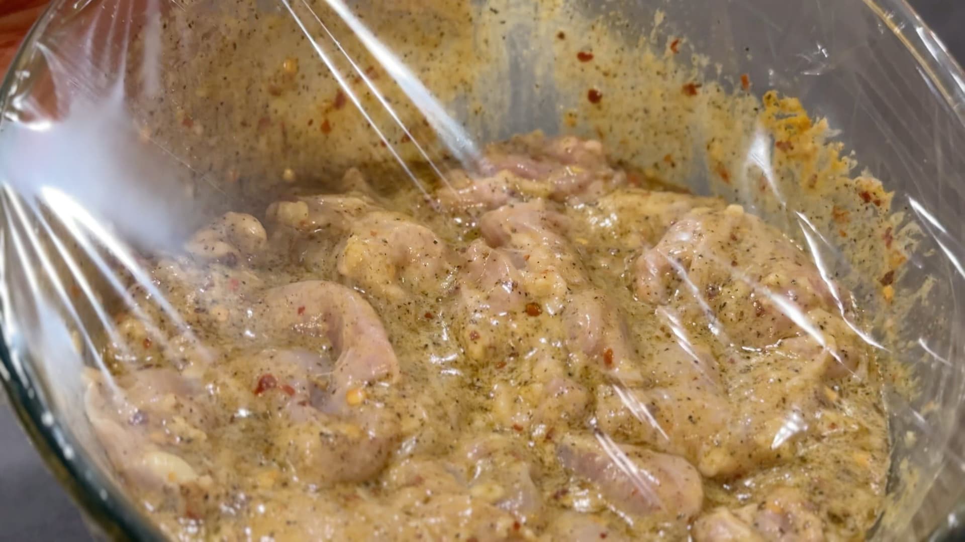 Chicken pieces marinating in yogurt and spices in a glass bowl with a whisk