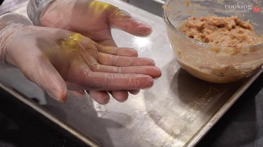 Hands shaping ground chicken mixture into nugget balls on parchment paper with bowl of mixture nearby.