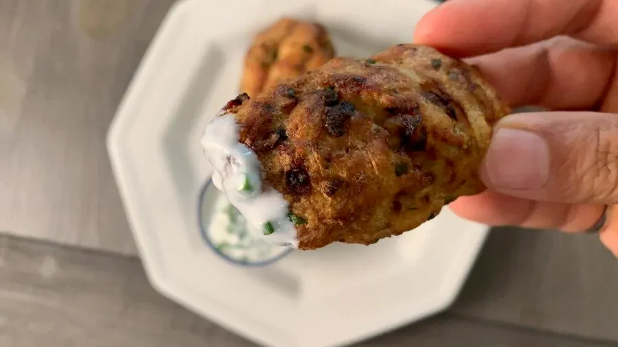 Hand holding a golden-brown crispy air fryer chicken cutlet with white sauce on a white plate.