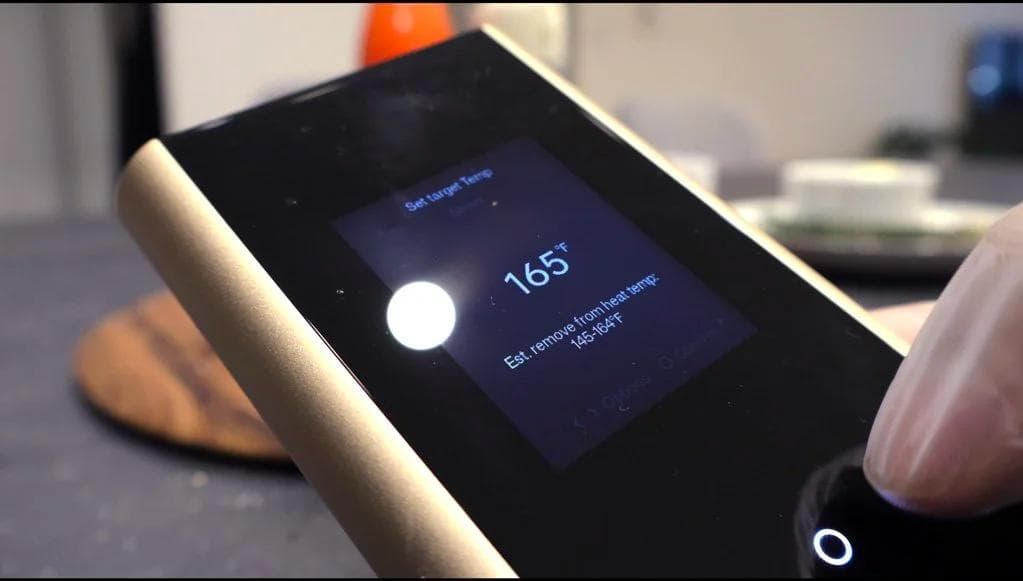 Smart meat thermometer displaying 165°F internal temperature during chicken cooking process.