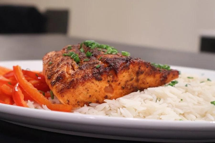 Air fryer salmon fillet with crispy spiced crust served over white rice with red bell peppers.
