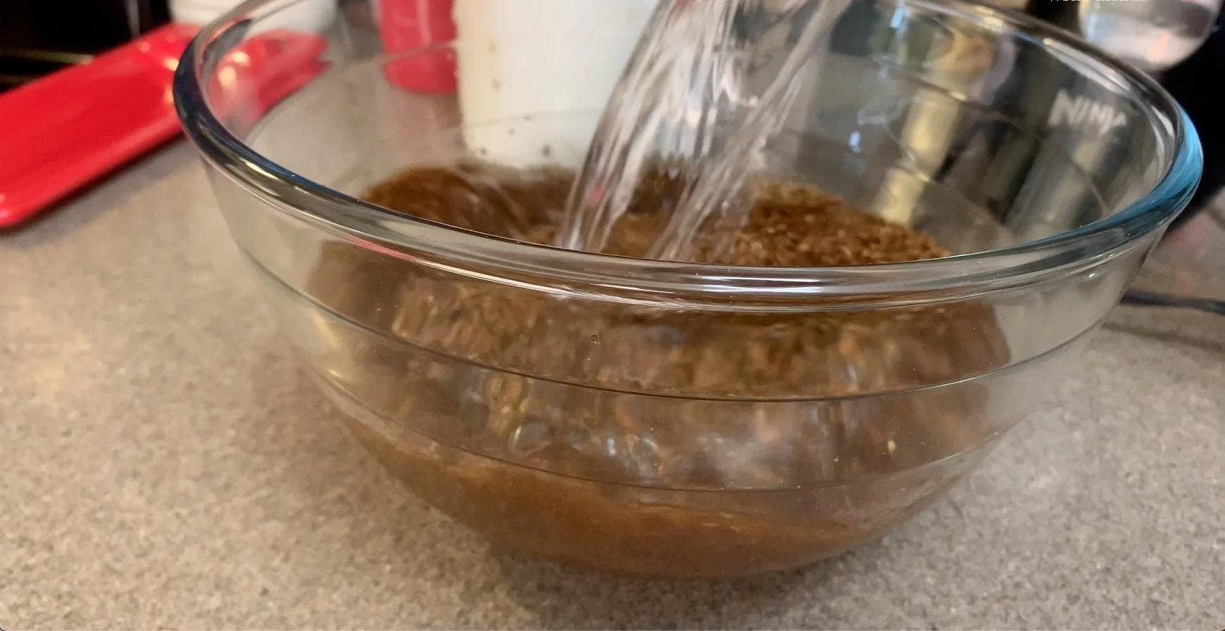 Ground coffee steeping in water in a glass bowl for cold brew preparation.