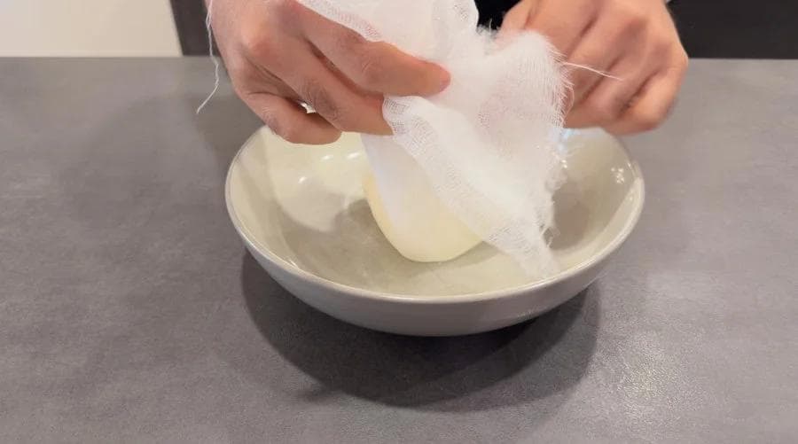 Hands wrapping yogurt-based tandoori marinade around chicken pieces in a white bowl.