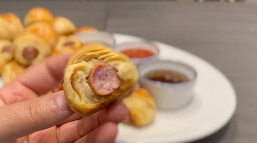 Hand holding a golden air fryer pig in a blanket with a slice of pepperoni visible inside the crescent roll.
