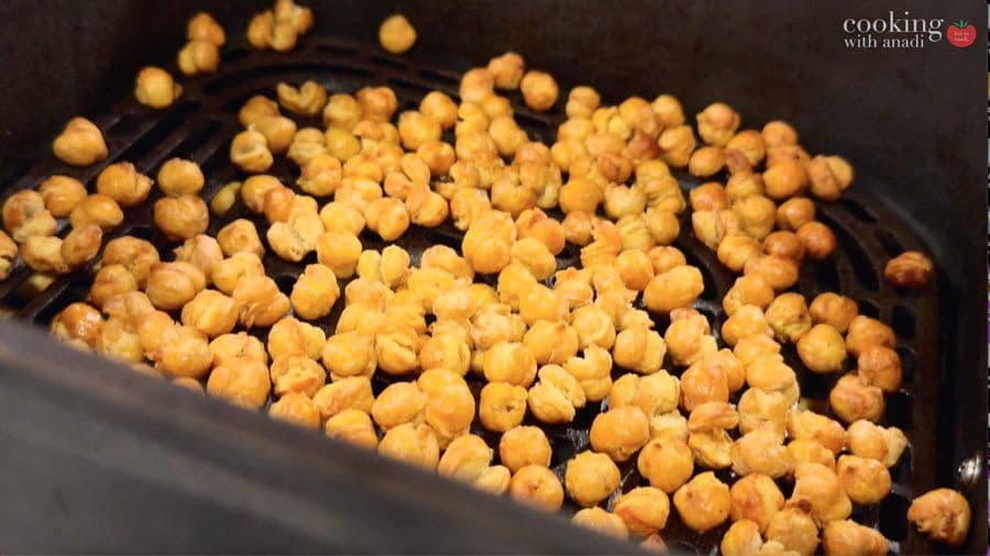 Golden crispy chickpeas in air fryer basket after cooking, ready for seasoning.