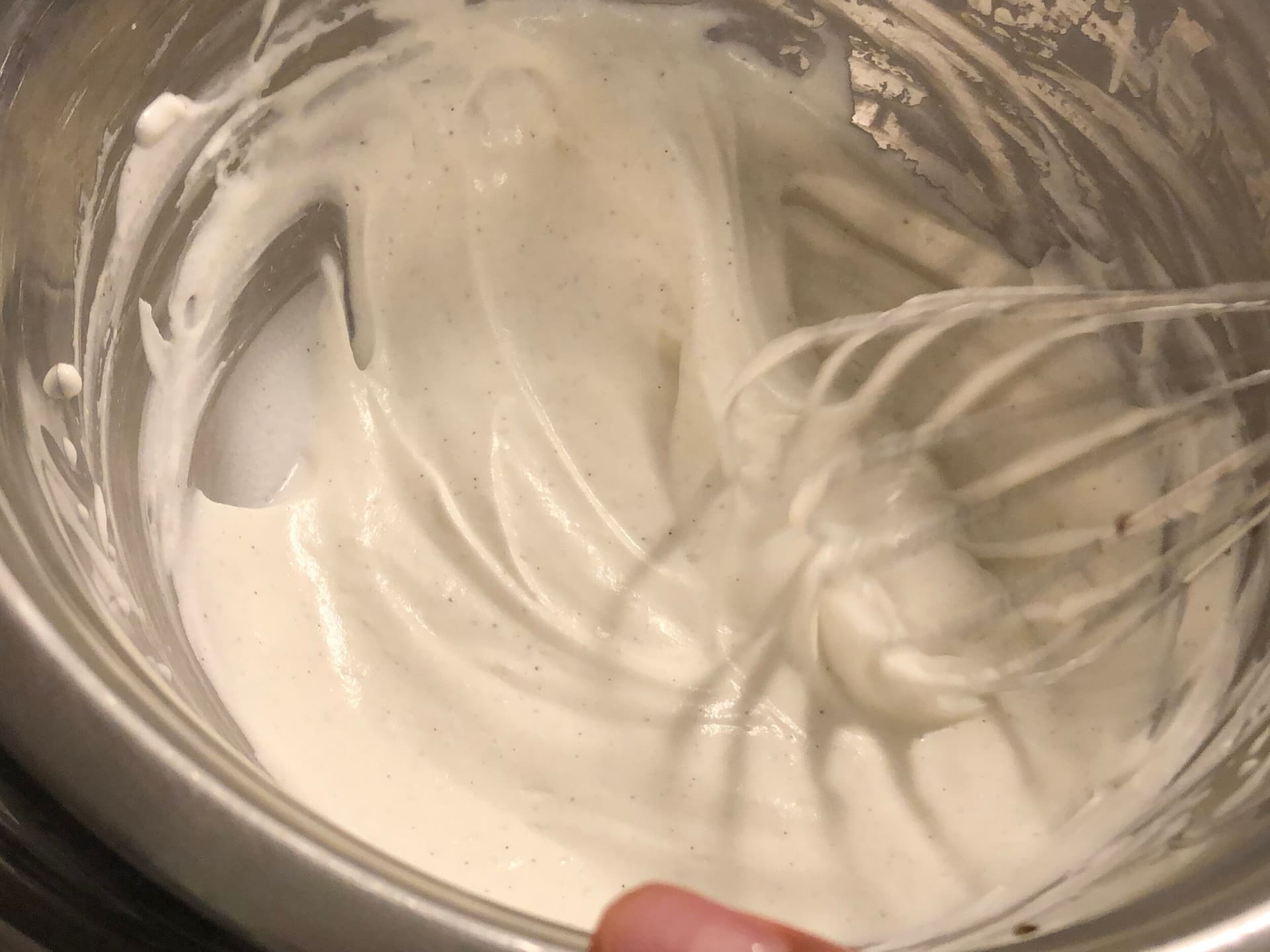 Whipped cream with soft peaks being lifted on a whisk in a glass bowl