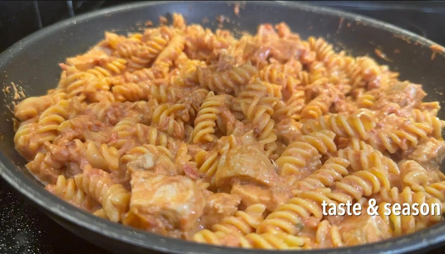 Creamy tomato chicken pasta with spinach mixed together in a pan, ready for parmesan cheese.