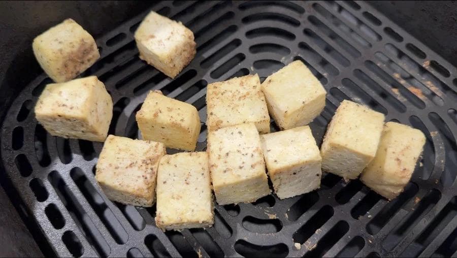 Seasoned tofu cubes spaced out in an air fryer basket, showing proper spacing for air circulation.