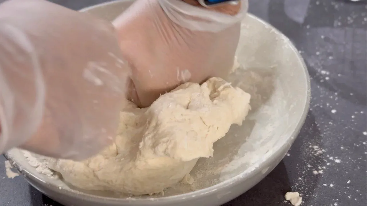 Hands kneading soft, pale dough in a white bowl during momo dough preparation.