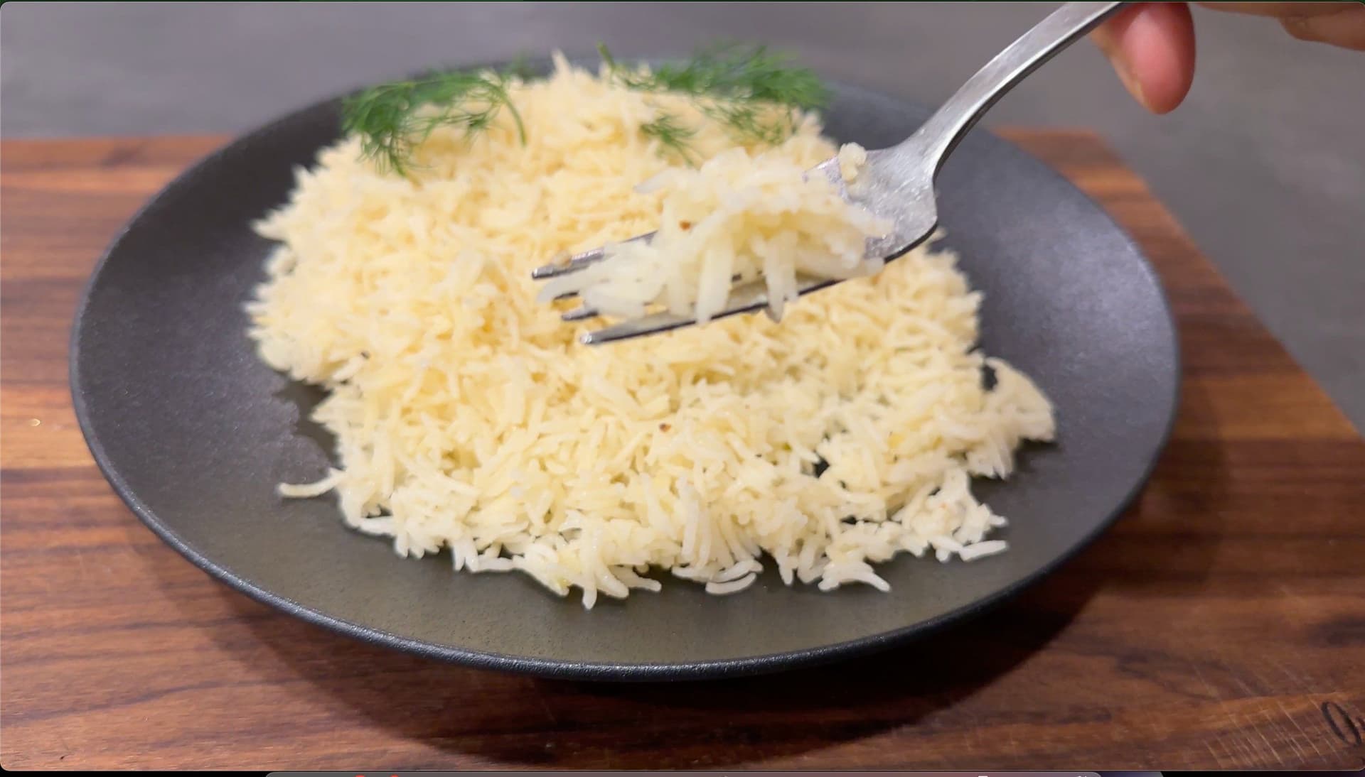 Fluffy Greek lemon rice pilaf on a dark plate, garnished with fresh dill, being fluffed with a fork.