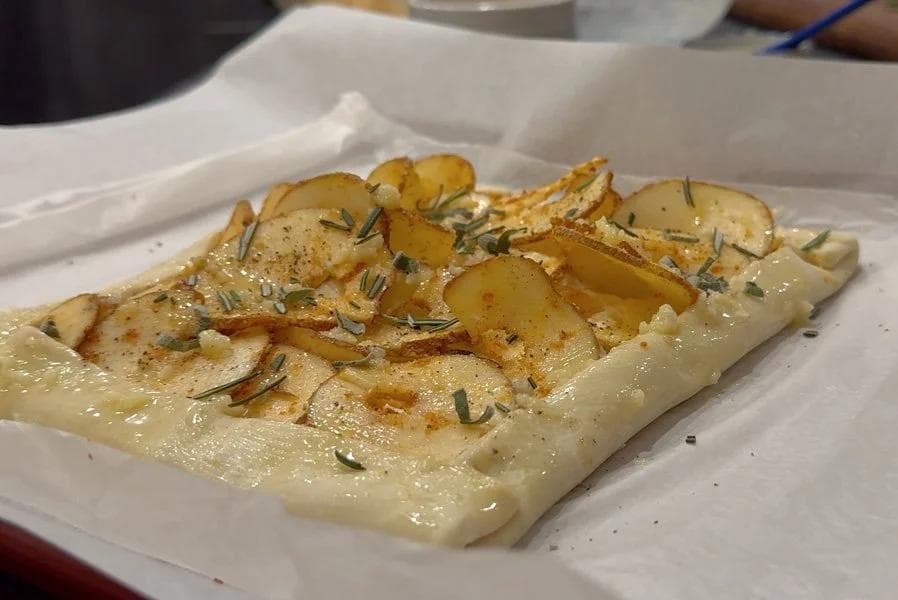 Baked puff pastry tart topped with sliced roasted potatoes, rosemary, and black pepper on a white plate.