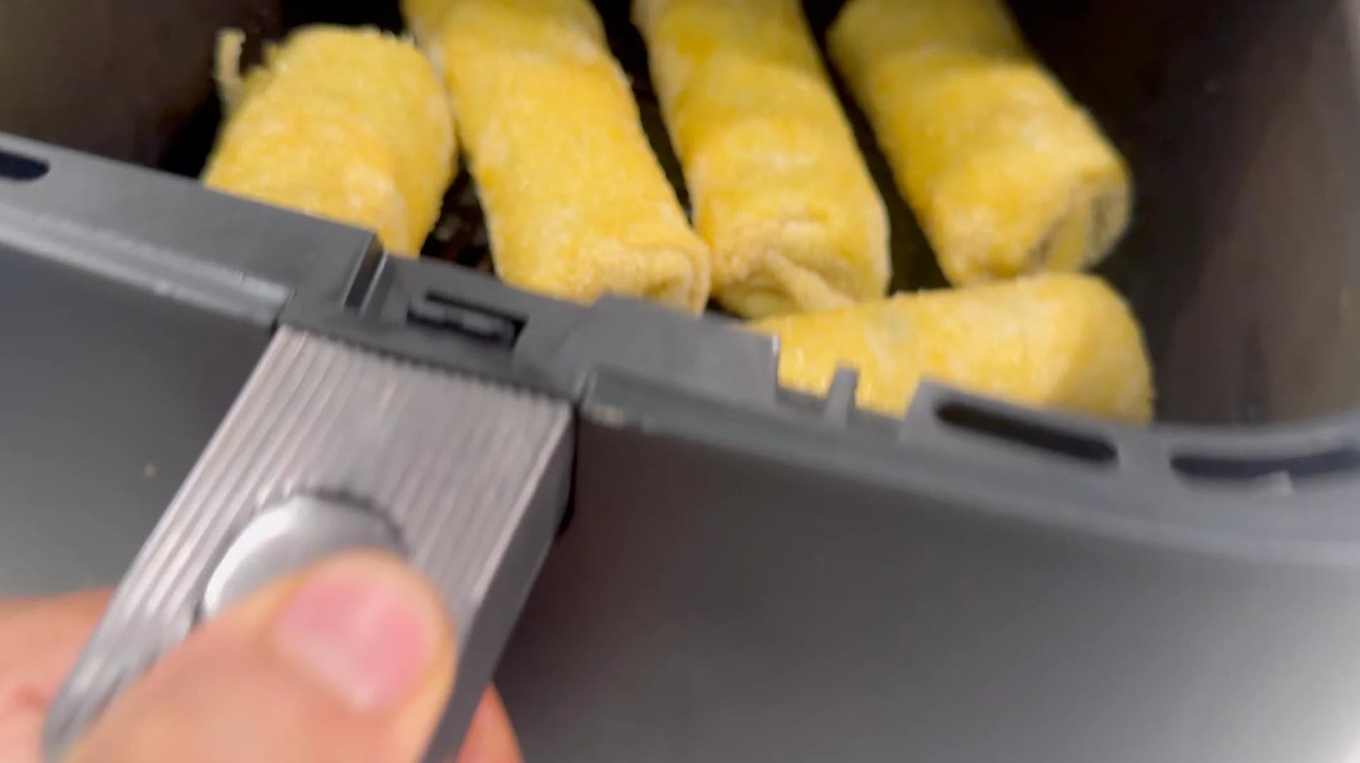 Breaded krokiety being brushed with melted butter before air frying in a gray air fryer basket.