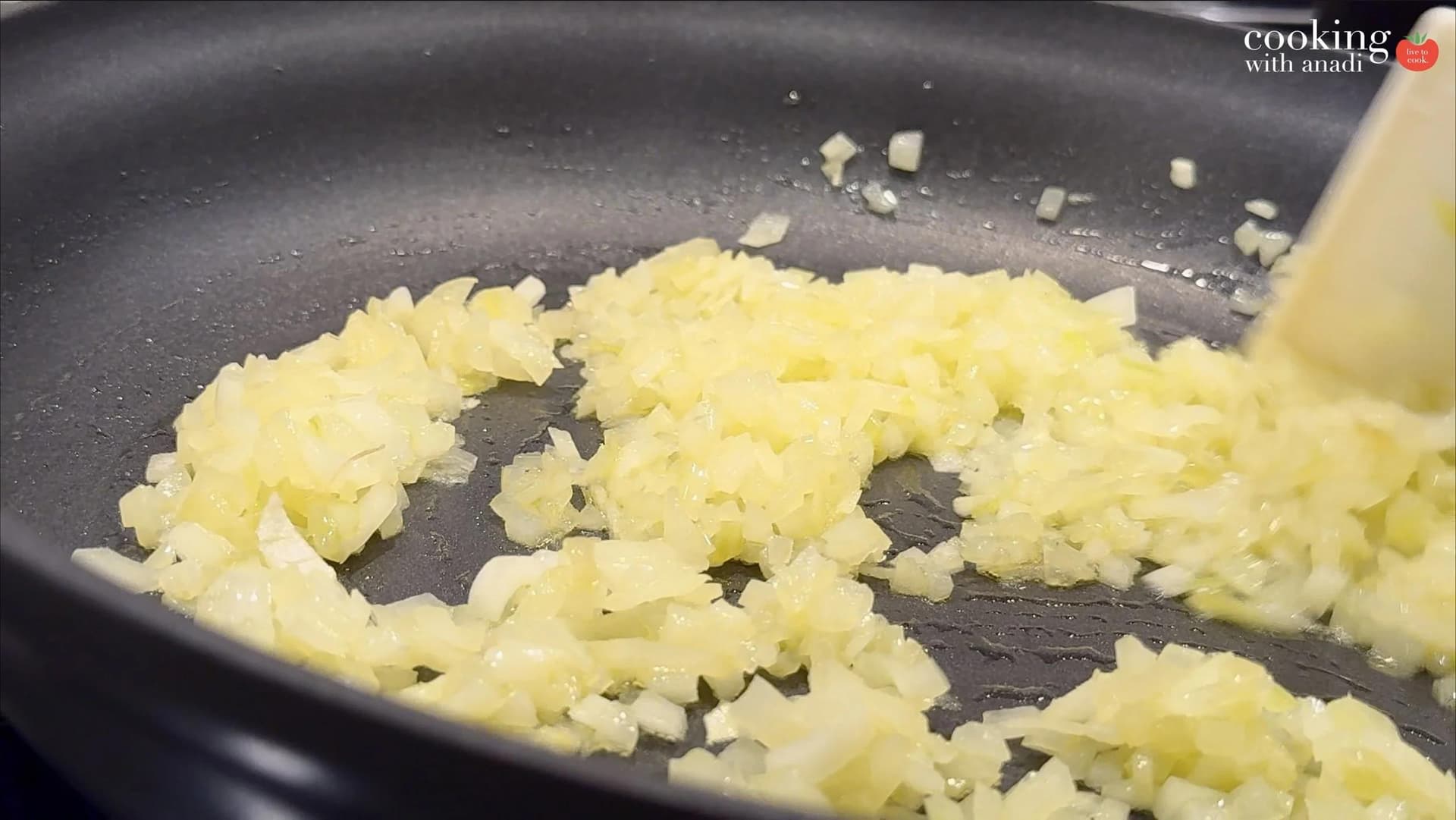 Diced onions sautéing in a dark nonstick skillet, softened and translucent, being stirred with a spatula.