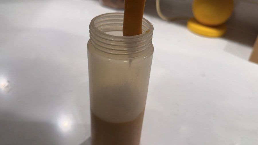 Osaka spicy umami sauce in a clear squeeze bottle, showing layered ingredients with a wooden spoon inside.