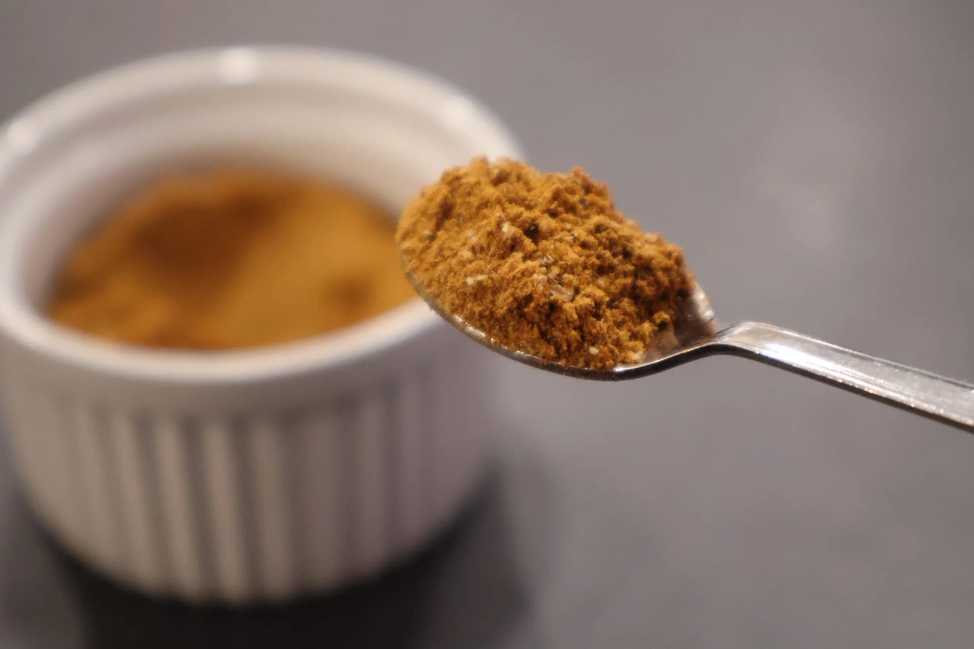 Homemade Nigerian curry powder on a spoon held above a bowl of stored curry powder.