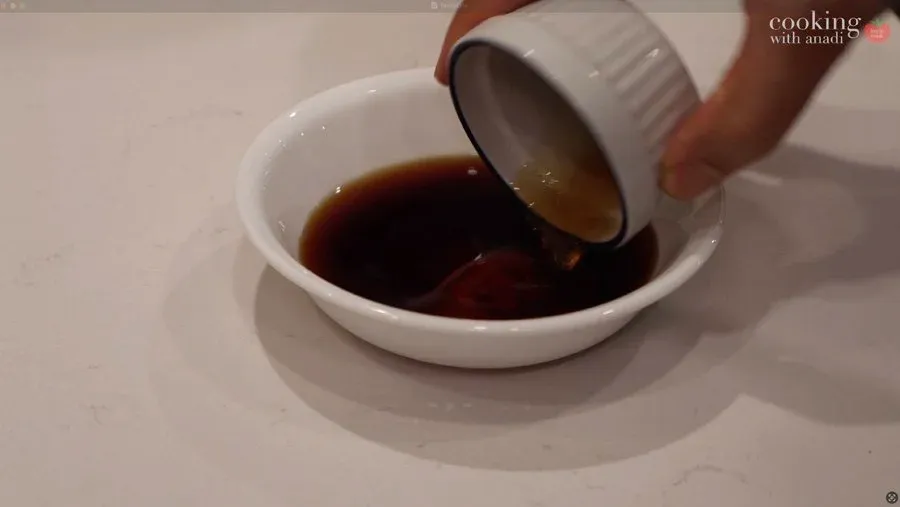 Dark brown stir fry sauce being poured from a small white bowl into a larger white bowl.