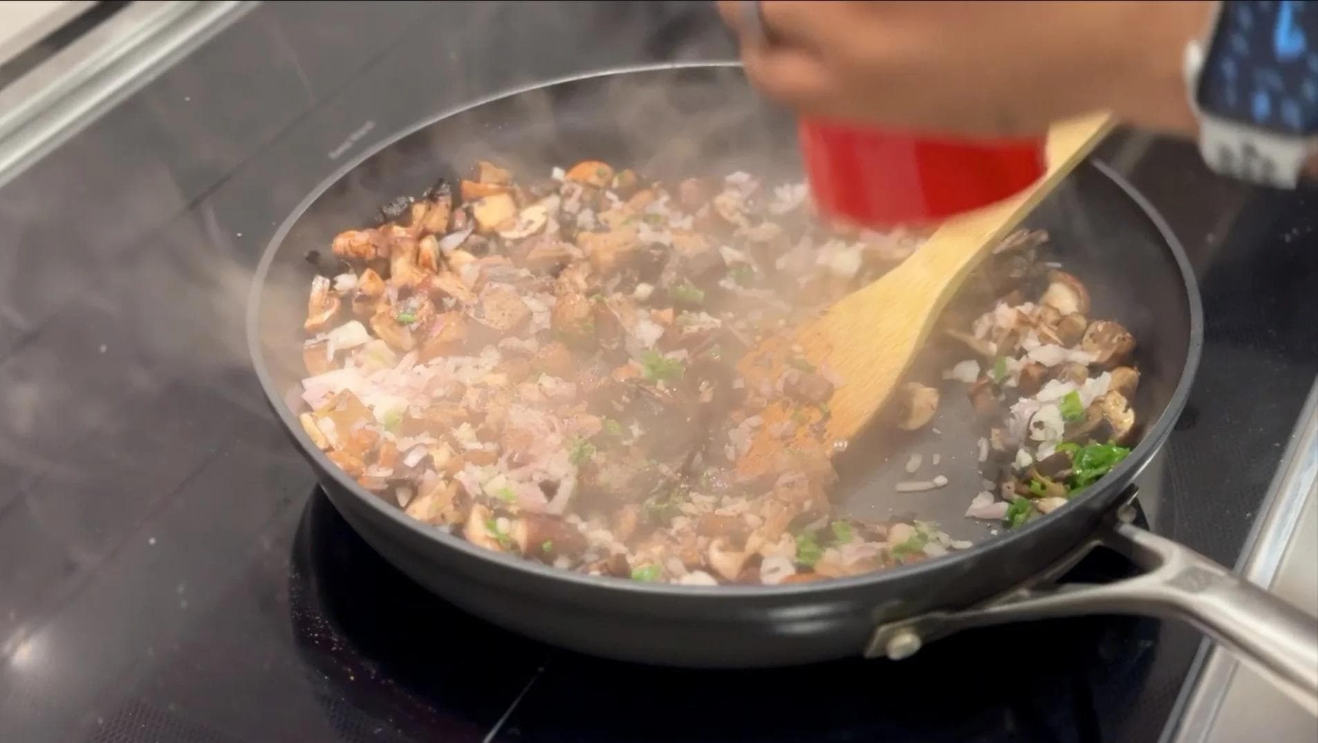 Sautéed mushrooms with shallots and garlic cooking in a skillet with a wooden spoon.