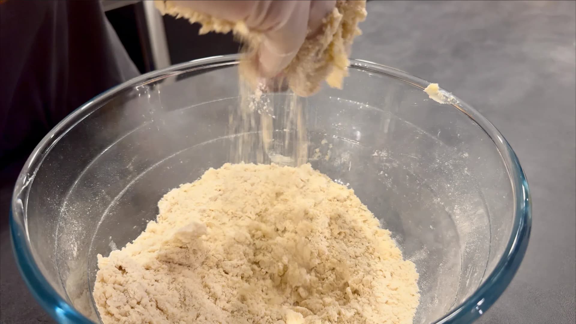 Pouring flour mixture into a glass bowl for Nigerian meat pie crust dough.