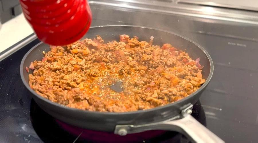 Cooked ground beef with spices in a skillet on the stovetop, partially browned and crumbled.