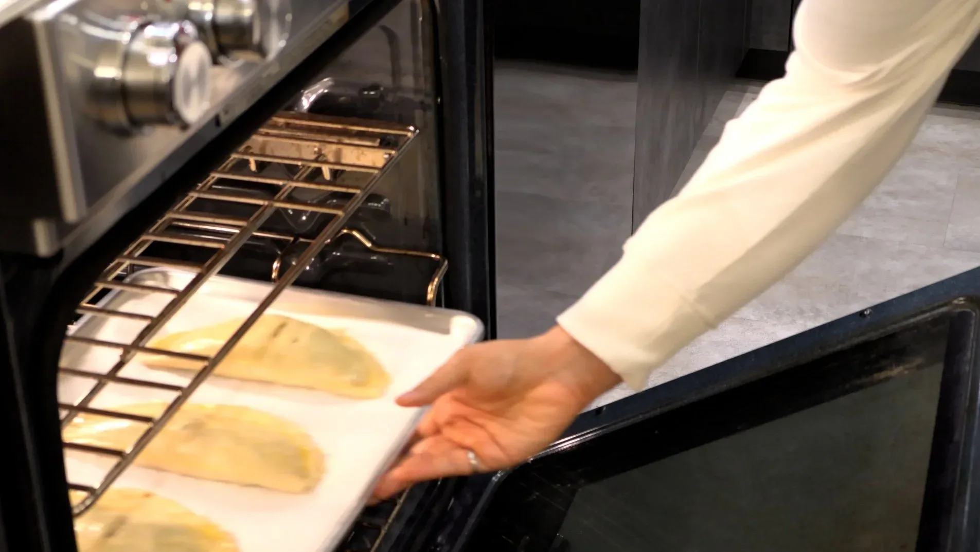 Hand brushing egg wash onto unbaked tourtiere pastries on a parchment-lined baking sheet in an oven.