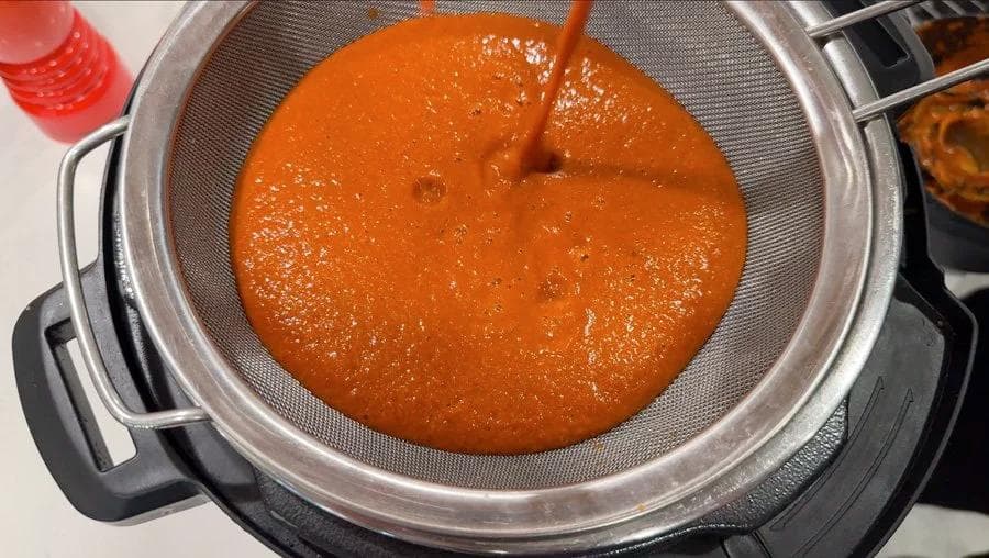 Red birria consommé being strained through a fine mesh sieve into a pot.