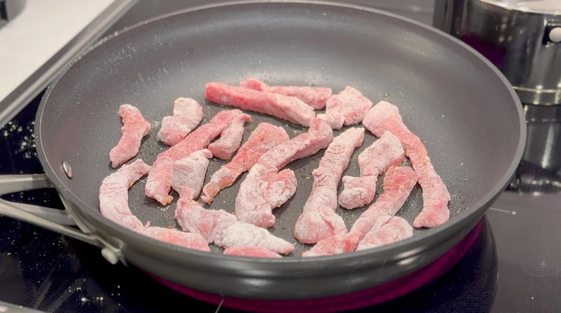 Breaded beef strips cooking in a pan on medium-high heat, partially browned on one side.