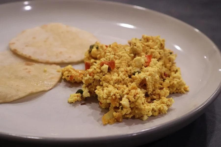 Paneer bhurji served on a white plate with two plain flatbreads, showing scrambled cottage cheese with red peppers and spices.