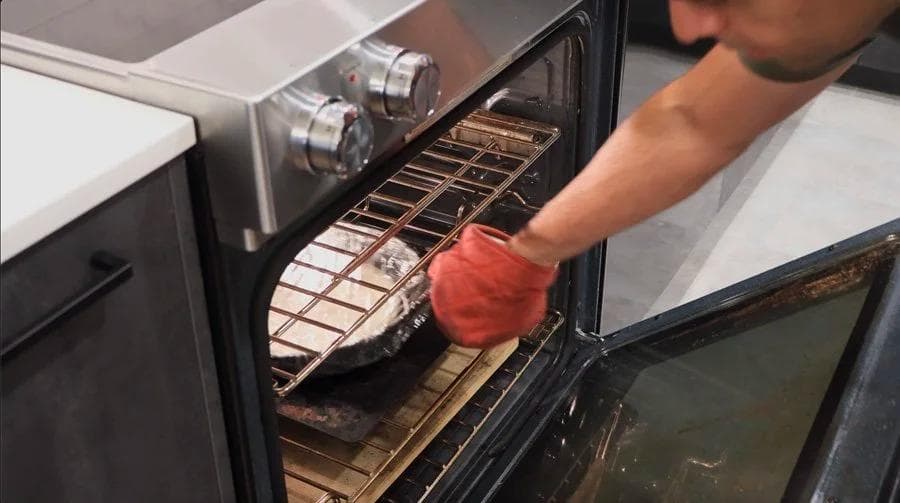 Person placing cast iron pan with pizza dough into preheated oven using red oven mitt.
