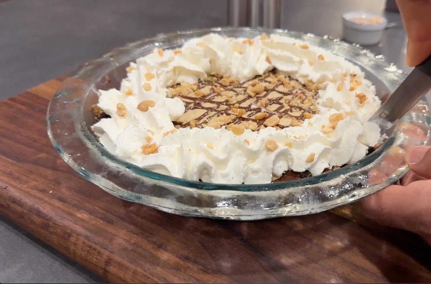 No-bake peanut butter pie topped with whipped cream, chopped peanuts, and chocolate drizzle in a glass pie dish.