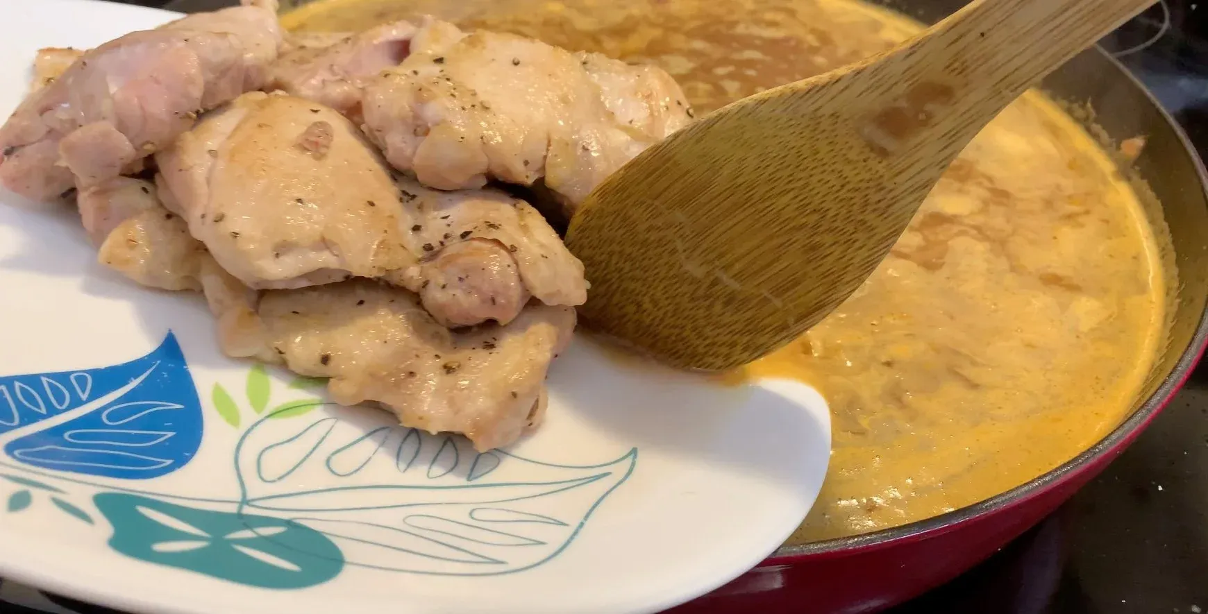 Cooked chicken pieces on a plate next to a pot of golden Moroccan stew being stirred with a wooden spoon.