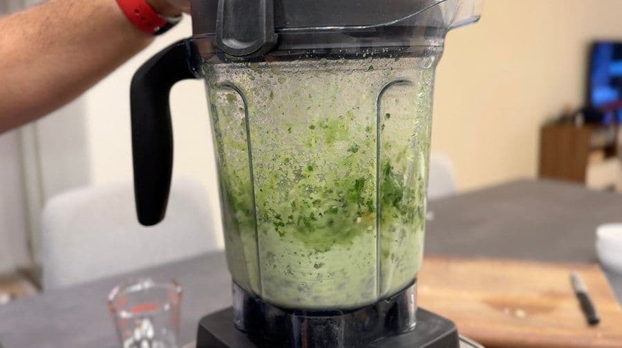 Blender filled with green amla chutney being puréed to smooth consistency.